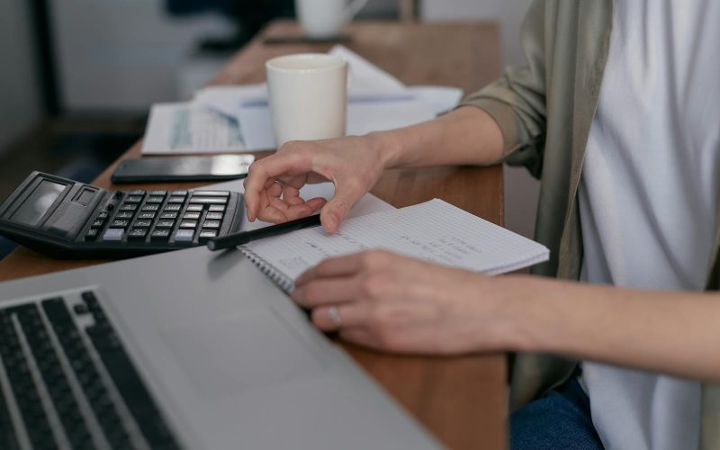 A mid-adult calculating finances with a laptop and notepad, managing budgets at home.